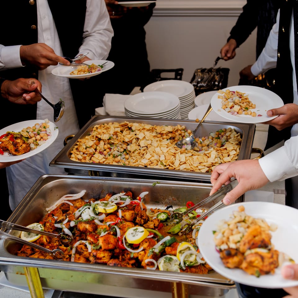 Guests serve themselves grilled chicken and chickpea salad from buffet trays at a restaurant gathering.